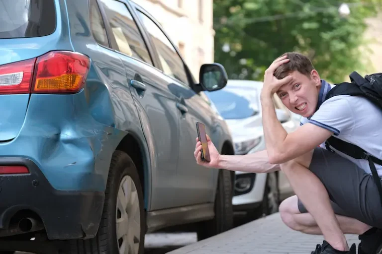 A young man holds his head in frustration while taking a photo of damage to his car's bumper after a hit-and-run in Alpharetta, GA.