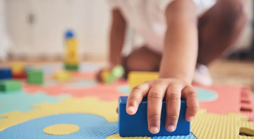 A child's hand is reaching for a blue foam puzzle piece on a colorful playmat which is highlighting daycare injury liability and supervision concerns in Georgia.