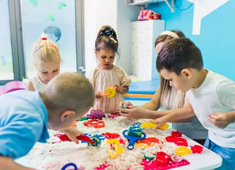A group of young children is playing with toys and sensory materials at a daycare table and is raising questions about daycare injury liability supervision in Georgia.
