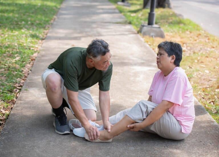 An older man kneels down to assist a woman sitting on a sidewalk who has injured her ankle after a fall depicting the type of trip and fall accident that commonly leads to a premises liability claim in Georgia.