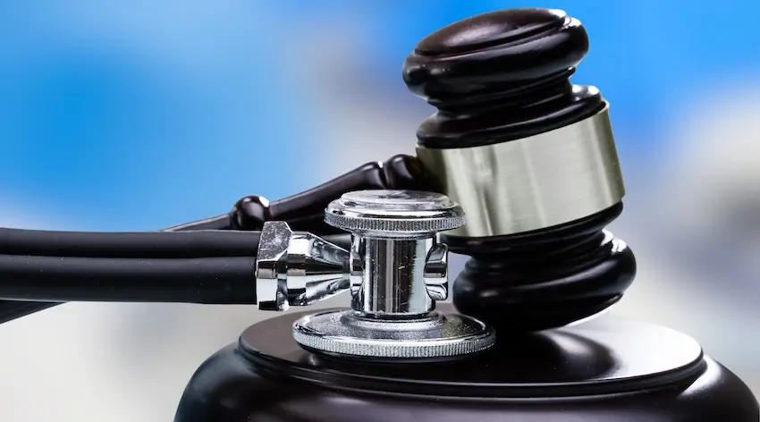 A dark wooden judge's gavel with a silver band rests directly on top of a chrome stethoscope chest piece on a black sound block against a blue background representing the critical role that medical documentation plays in connecting clinical evidence to legal outcomes in personal injury cases with help from Hartley Rowe & Fowler P.C.