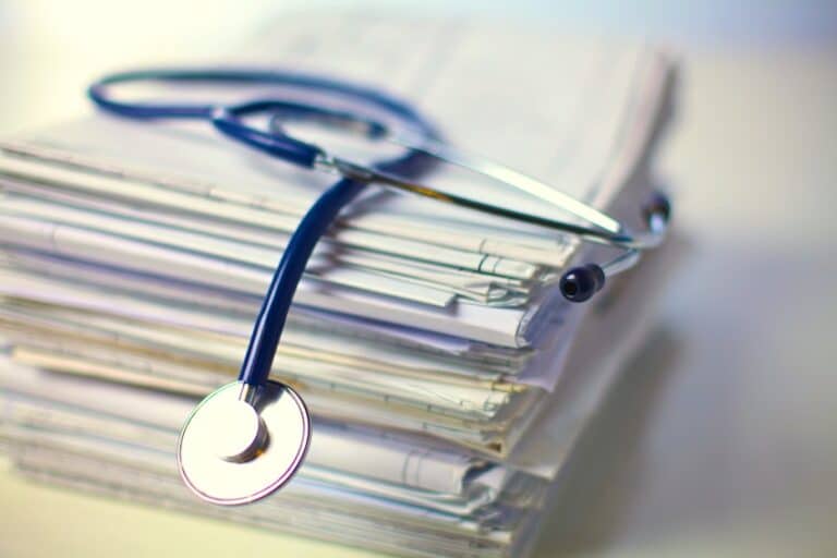 A blue stethoscope draped over a tall stack of papers and medical files on a softly lit surface depicting the extensive volume of medical documentation that accumulates during a serious injury victim's treatment and that attorneys from Hartley Rowe & Fowler P.C. rely on to build a strong compensation claim in Georgia.